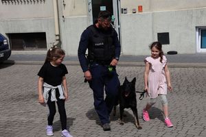 Na zdjeciu uczniowie SP nr 28 w Rzeszowie z wizytą w rzeszowskiej komendzie. Na środku idzie  policjant przewodnik psa, jego pies przy nim. Z prawej i lewej strony idą dziewczynki.