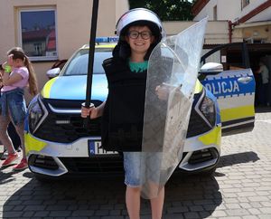Na zdjeciu chłopiec w policyjnej kamizelce  kamienioodpornej, na głowie ma założony kask, w ręce trzyma tarczę.