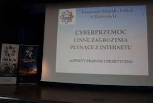 Na zdjęciu ekran z napisem Komenda Miejska Policji w Rzeszowie cyberprzemoc i inne zagrożenia płynące z internetu aspekty prawne i praktyczne. W górnym lewym rogu policyjna odznaka.