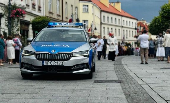 Na zdjęciu policyjny radiowóz w tle procesja.