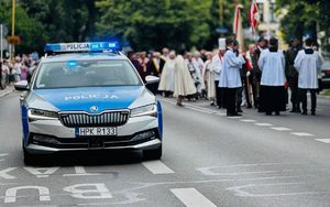 Na zdjęciu policyjny radiowóz w tle procesja.