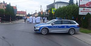 Na zdjęciu policyjny radiowóz,  w tle procesja.