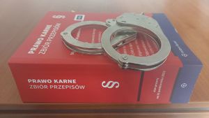 Na zdjęciu zbiór przepisów karnych, na nim leżą policyjne kajdanki.