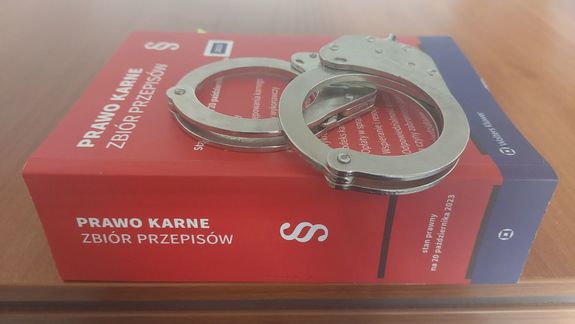 Na zdjęciu zbiór przepisów karnych, na nim leżą policyjne kajdanki.