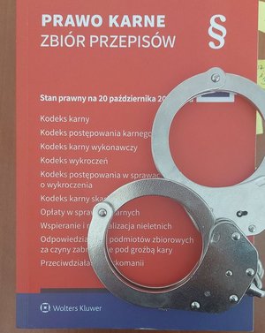 Na zdjęciu kodeks postępowania karnego i policyjne kajdanki.