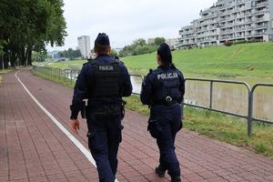 Na zdjęciu stoi odwróconych tyłem dwoje umundurowanych funkcjonariuszy policji, przed nimi rzeka.