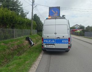 Na zdjeciu policyjny ambulans ruchu drogowego z wysunięta tablica świtelną informująca o wypadku. Po lewej stronie w rowie motocykl.