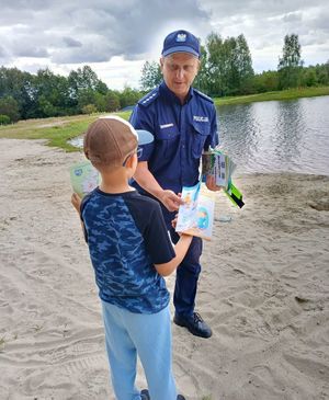 Na zdjeciu umundurowany policjant i chłopiec, w tle zalew.