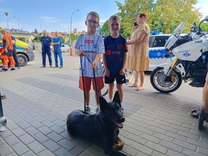 Na zdjęciu dwóch chłopców, jeden z nich trzyma na smyczy czarnego psa.