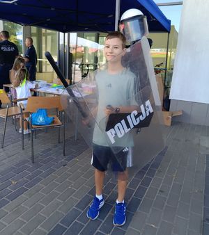 Na zdjeciu chłopiec trzyma w ręce policyjną tarczę i palkę.