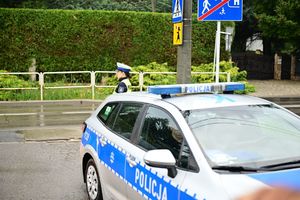 Na zdjeciu umundurowana policjanta ruchu drogowego, obok niej policyjny radiowóz.