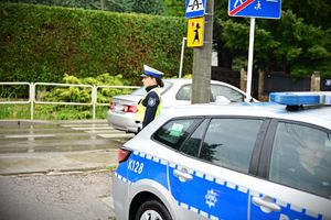 Na zdjeciu umundurowana policjanta ruchu drogowego, obok niej policyjny radiowóz.
