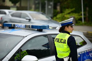 Na zdjeciu umundurowana policjanta ruchu drogowego, obok niej policyjny radiowóz.
