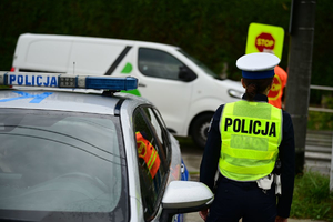 Na zdjeciu umundurowana policjanta ruchu drogowego, obok niej policyjny radiowóz.