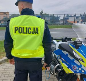 Na zdjęciu umundurowany policjant ruchu drogowego. Obok niego policyjny motocykl.