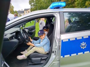 Na zdjęciu siedzące w radiowozie dwie dziewczynku, na głowach mają policyjne czapki.