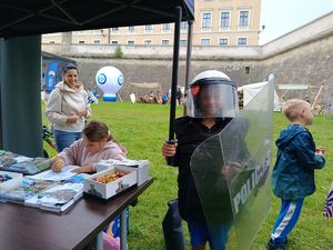 Na zdjęciu chłopiec w policyjnym kasku, w ręce trzyma tarcze i pałkę.