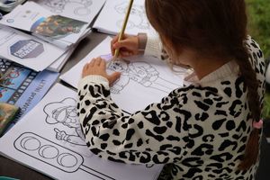 Na zdjeciu przy stoliku siedzi dziewczynka i koloruje obrazek policjanta.