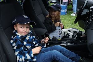 Na zdjeciu policyjny radiowóz, na przednich siedzeniach siedzą dzieci, na głowach mają policyjne czapki.