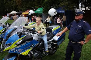 Na zdjeciu policyjny motocykl na którym siedzi chłopiec, obok stoi umundurowany policjant.