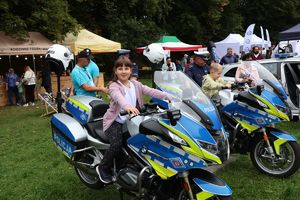 Na zdjęciu dwa policyjne motory, na jednym siedzi dziewczynka, na drugim chłopiec. Z boki stoi umundurowany policjant.