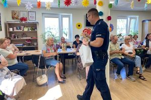 Na zdjęciu umundurowany policjant, na krzesełkach siedzą seniorzy.