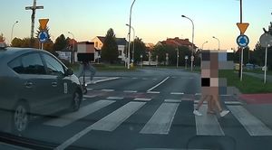 Na zdjeciu przejście dla pieszych. Na lewym pasek widać jadącego na hulajnodze mężczyznę, w którego wjeżdża pojazd, na prawym pasie idą dwie osoby.
