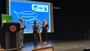 Na zdjęciu umundurowana policjantka z mikrofonem w ręce.Za nią na multimedialnej tablicy napis porozmawiajmy o bezpieczeństwie-możesz mieć n nie wpływ., w towarzystwie organizatorów spotkania.