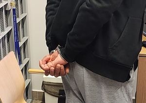 Na zdjęciu mężczyzna z założonym na ręce trzymane z tyłu kajdankami.