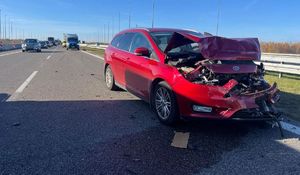 Na zdjęciu uszkodzony pojazd koloru czerwonego, w tle policyjny radiowóz.