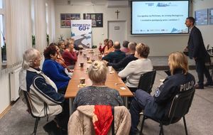 Na zdjeciu umundurowana policjantka siedzi przy stole wraz z seniorami.