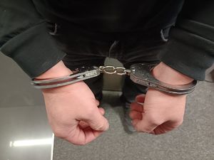 Na zdjęciu osoba w ciemnej kurtce, która na ręce ma założone kajdanki.