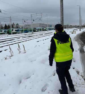 Na zdjęciu umundurowany policjant w żółtej kamizelce odblaskowej z napisem policja na plecach.