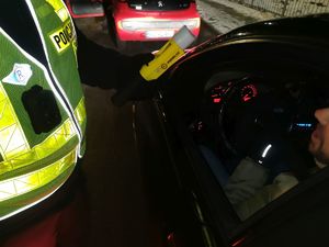 Na zdjęciu umundurowany policjant w żółtej odblaskowej kamizelce podczas kontroli stanu trzeźwości kierującego.