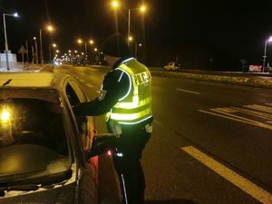 Na zdjęciu umundurowany policjant w żółtej odblaskowej kamizelce podczas kontroli stanu trzeźwości kierującego.