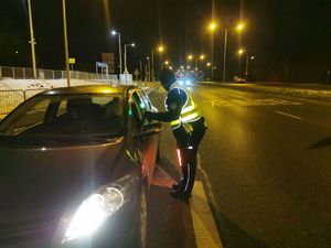 Na zdjęciu umundurowany policjant w żółtej odblaskowej kamizelce podczas kontroli stanu trzeźwości kierującego.