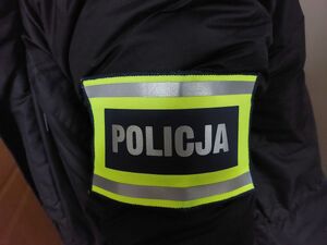Na zdjęciu naramienna opaska odblaskowa z napisem policja na czarnym tle.