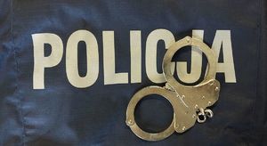 Na zdjęciu policyjna bluza służbowa z napisem policja, na niej leżą kajdanki.