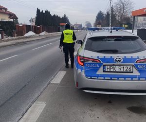 Na zdjęciu umundurowana policjantka, obok niej radiowóz.