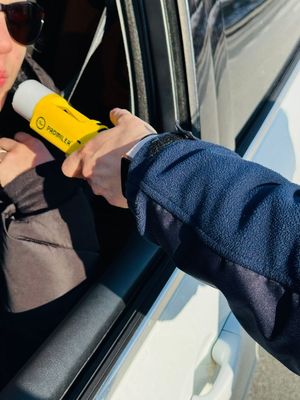 Na zdjęciu umundurowana policjantka ruchu drogowego podczas kontroli stanu trzeźwości kierującego pojazdem.