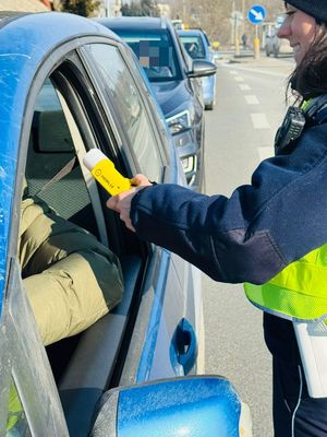 Na zdjęciu umundurowana policjantka ruchu drogowego podczas kontroli stanu trzeźwości kierującego pojazdem.