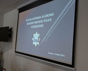Na zdjęciu tablica multimedialna na której jest slajd z napisem roczna odprawa służbowa w Komendzie Miejskiej Policji w Rzeszowie.