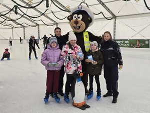 Na zdjęciu policyjny miś POPO, policjantki oraz dzieci korzystające z lodowiska.