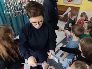 Na zdjęciu dzielnicowa rozdająca dzieciom odblaski.