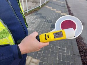 Na zdjęciu policjant trzymający w ręku urządzenie do badania stanu trzeźwości i tarczę do zatrzymywania pojazdów.