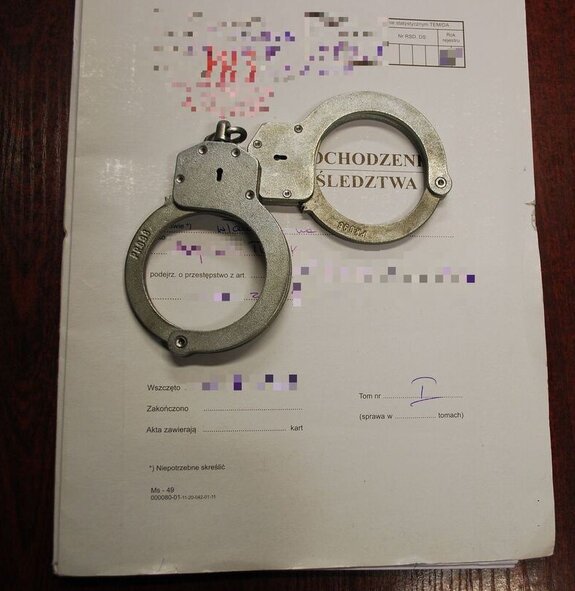 Na zdjęciu obwoluta na policyjne akta, na nich leżą kajdanki.