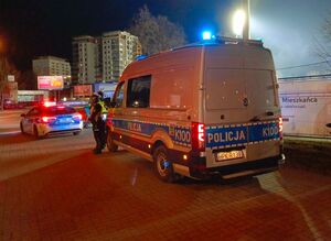 Na zdjeciu dwa policyjne radiowozu oraz dwóch umundurowanych policjantów ruchu drogowego.
