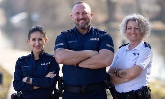 Na zdjęciu troje umundurowanych policjantów, dwie kobiety, pośrodku nich uśmiechnięty mężczyzna.