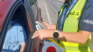 Na zdjeciu umundurowany policjant kontroluje stan trzeźwości siedzącego za kierownicą samochody kierowcy.