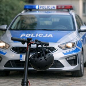 Na zdjeciu policyjny radiowóz, przed nim hulajnoga elektryczna, na kierownicy wisi kask.